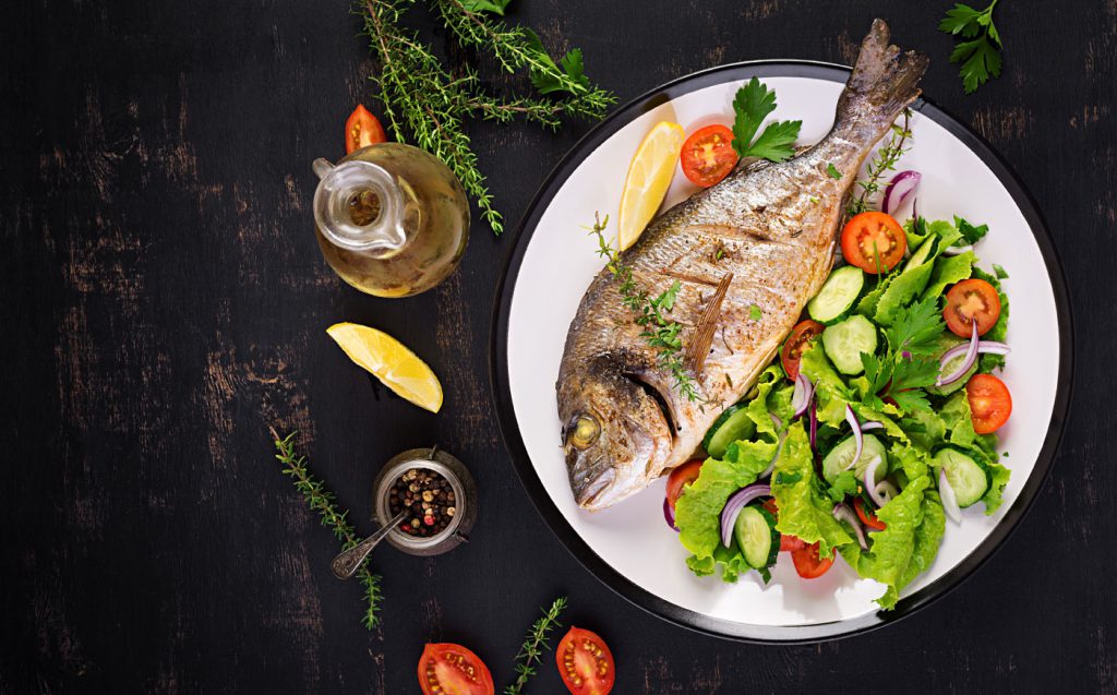 Gebackener Fisch mit Zitrone frischer Salat weiße Platte dunklen rustikalen Hintergrund Draufsicht gesundes Abendessen mit Fischrestaurant Rogoznica