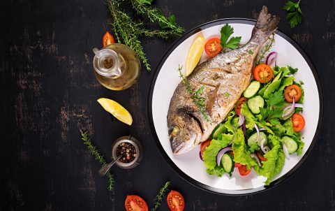 Baked fish with lemon fresh salad white plate dark rustic background top view healthy dinner with fish restaurant rogoznica