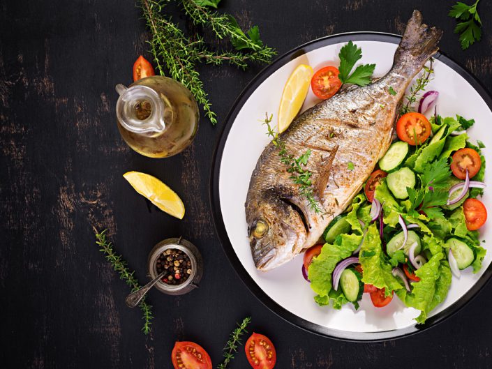 Gebackener Fisch mit Zitrone frischer Salat weiße Platte dunklen rustikalen Hintergrund Draufsicht gesundes Abendessen mit Fischrestaurant Rogoznica